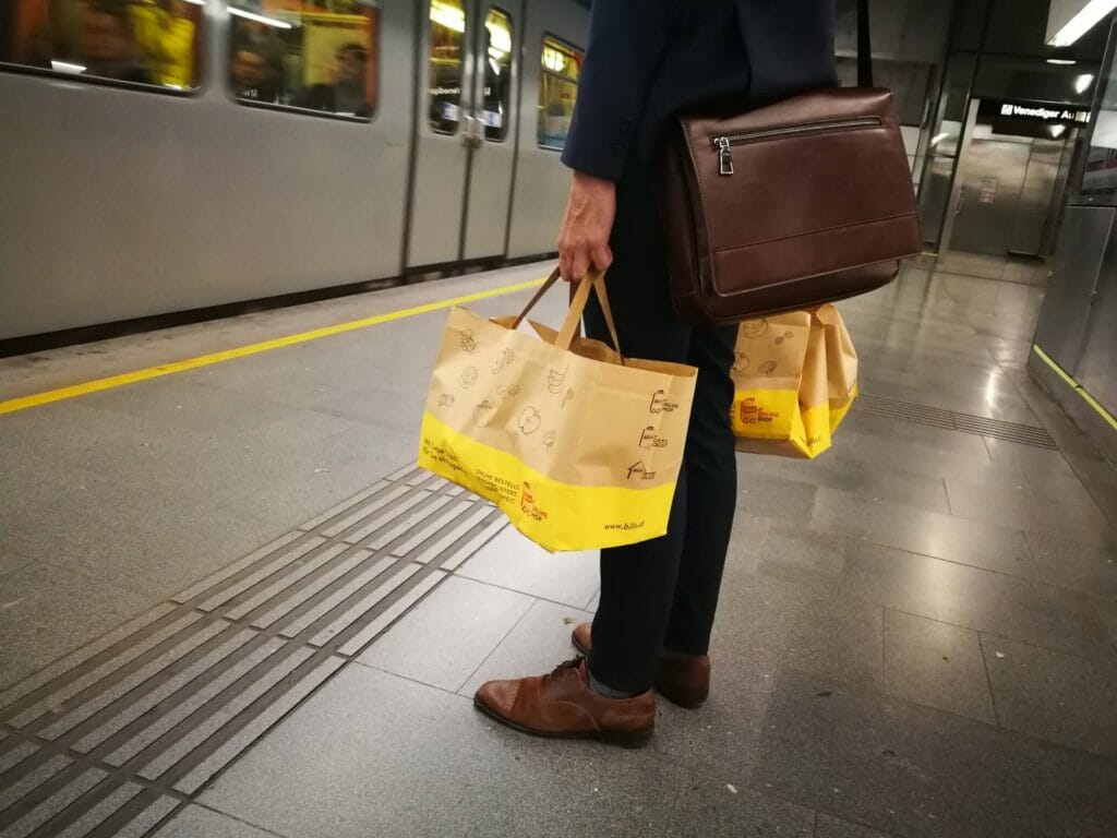 Zwei Tragetaschen/ Einkaufstaschen des BILLA Online Shops getragen von Businessmann in U-Bahn auf Bahnsteig